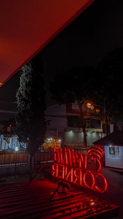 A vibrant neon box sign glowing brightly outside a cozy Surabaya cafe at dusk.