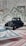 A vintage black toy car is placed on top of various pieces of currency and financial documents in different colors, including green and red. The background is filled with out-of-focus financial paperwork, creating a context of finance or wealth.