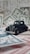 A vintage black toy car is placed on top of various pieces of currency and financial documents in different colors, including green and red. The background is filled with out-of-focus financial paperwork, creating a context of finance or wealth.