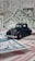 A vintage black toy car is placed on top of various pieces of currency and financial documents in different colors, including green and red. The background is filled with out-of-focus financial paperwork, creating a context of finance or wealth.