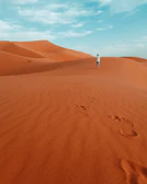 A winding desert trail with footprints leading toward distant rocky cliffs under a vibrant sky.