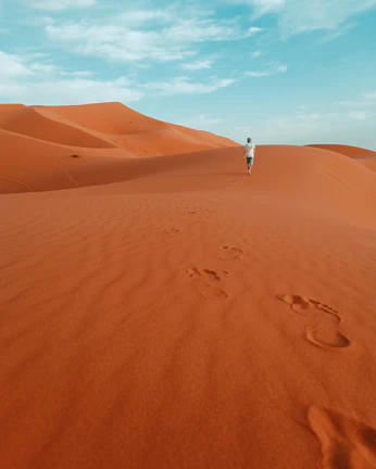 A winding desert trail with footprints leading toward distant rocky cliffs under a vibrant sky.