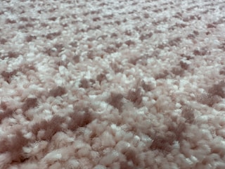 A close-up view of a fluffy, textured carpet with a blend of soft fibers. The surface is thick and plush, showcasing a uniform pattern with a slightly irregular arrangement that gives a sense of depth.