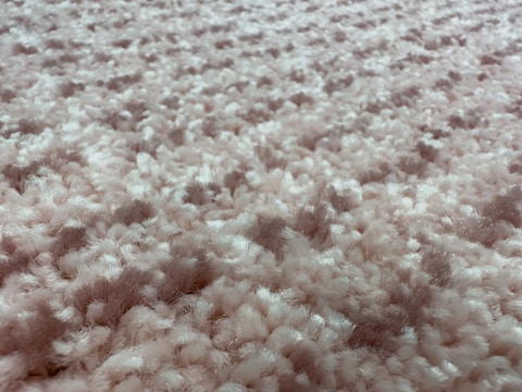 A close-up view of a fluffy, textured carpet with a blend of soft fibers. The surface is thick and plush, showcasing a uniform pattern with a slightly irregular arrangement that gives a sense of depth.