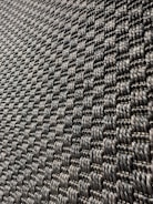 A close-up view of a textured surface with a woven pattern. The image captures a series of interlocking, dark-colored fibers that create a repetitive, geometric design with a slight shine under light.