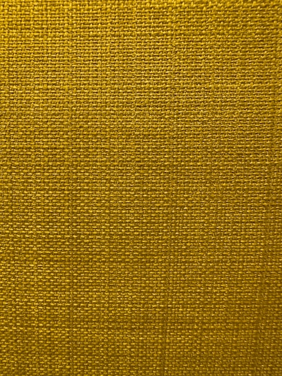 A close-up view of a textured fabric surface with a tight and even weave. The fabric appears to be made of thick threads, tightly interwoven in a grid pattern.