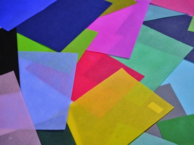 A collection of colorful, overlapping translucent sheets in a variety of shapes and sizes. The sheets include colors like red, yellow, blue, green, pink, and purple, creating a vibrant and dynamic visual effect.