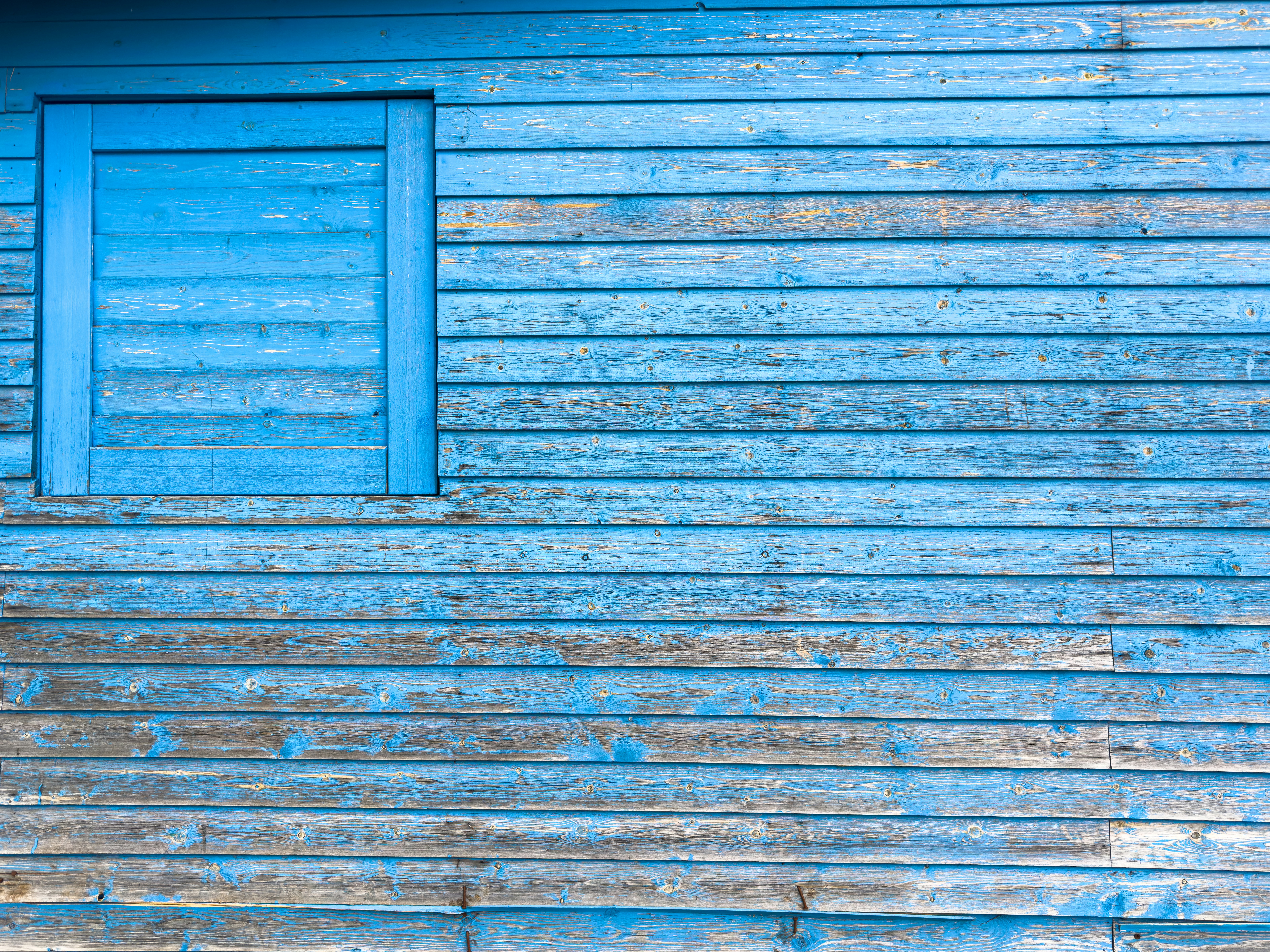 a blue wooden building with a window and a bench