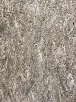 A detailed close-up of a wooden textured surface composed of compressed wood shavings and strands, exhibiting a rough and uneven pattern.