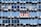 Rows of rectangular windows on a building facade, each equipped with air conditioning units. A sign with text in Spanish appears on one of the windows, indicating a space for rent. The windows vary in shades of blue, adding a uniform and repetitive architectural pattern.