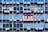 Rows of rectangular windows on a building facade, each equipped with air conditioning units. A sign with text in Spanish appears on one of the windows, indicating a space for rent. The windows vary in shades of blue, adding a uniform and repetitive architectural pattern.