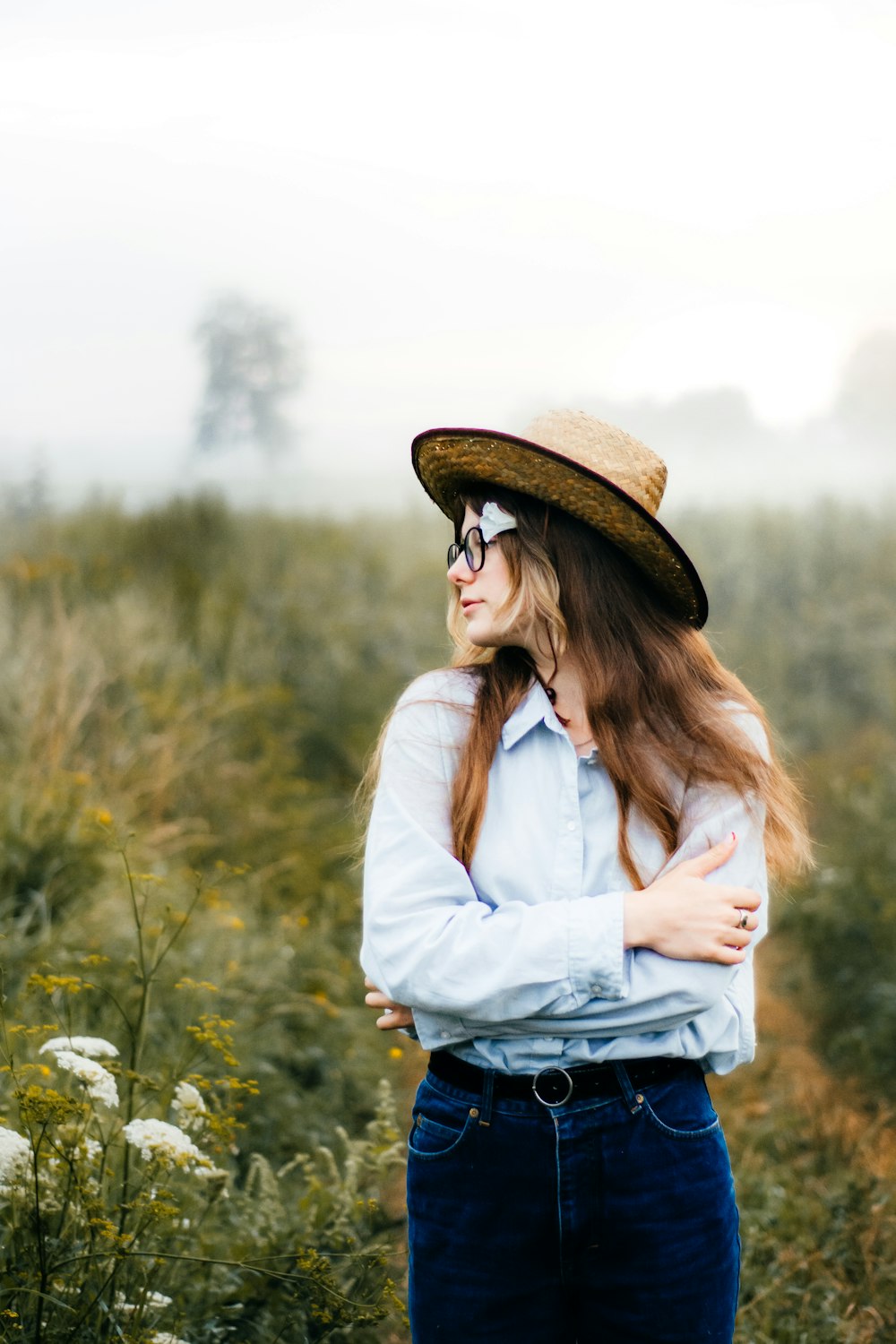 a woman wearing a hat and glasses standing in a field
