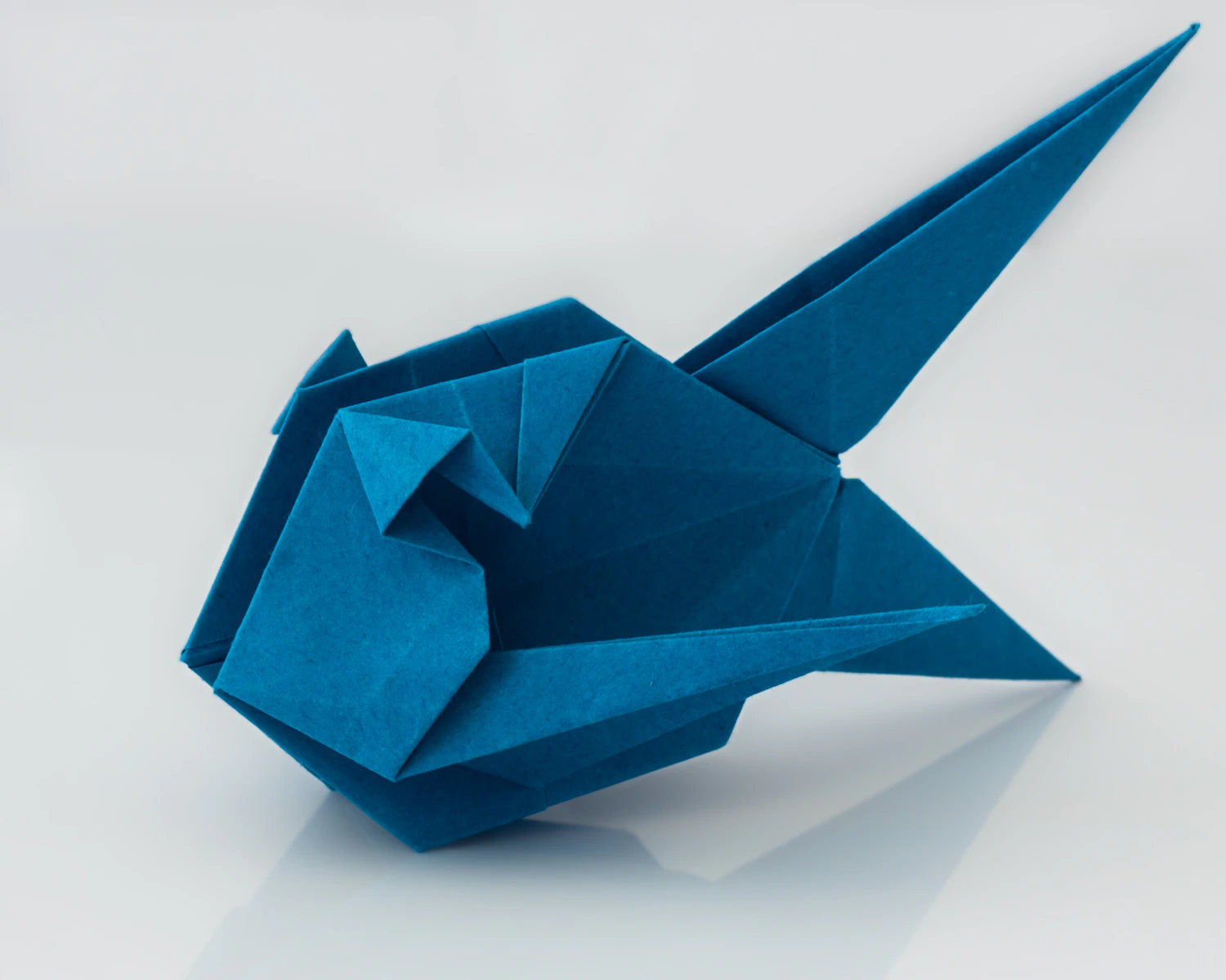 A deep indigo origami fish folded from one square of Ai-zome kami, on white