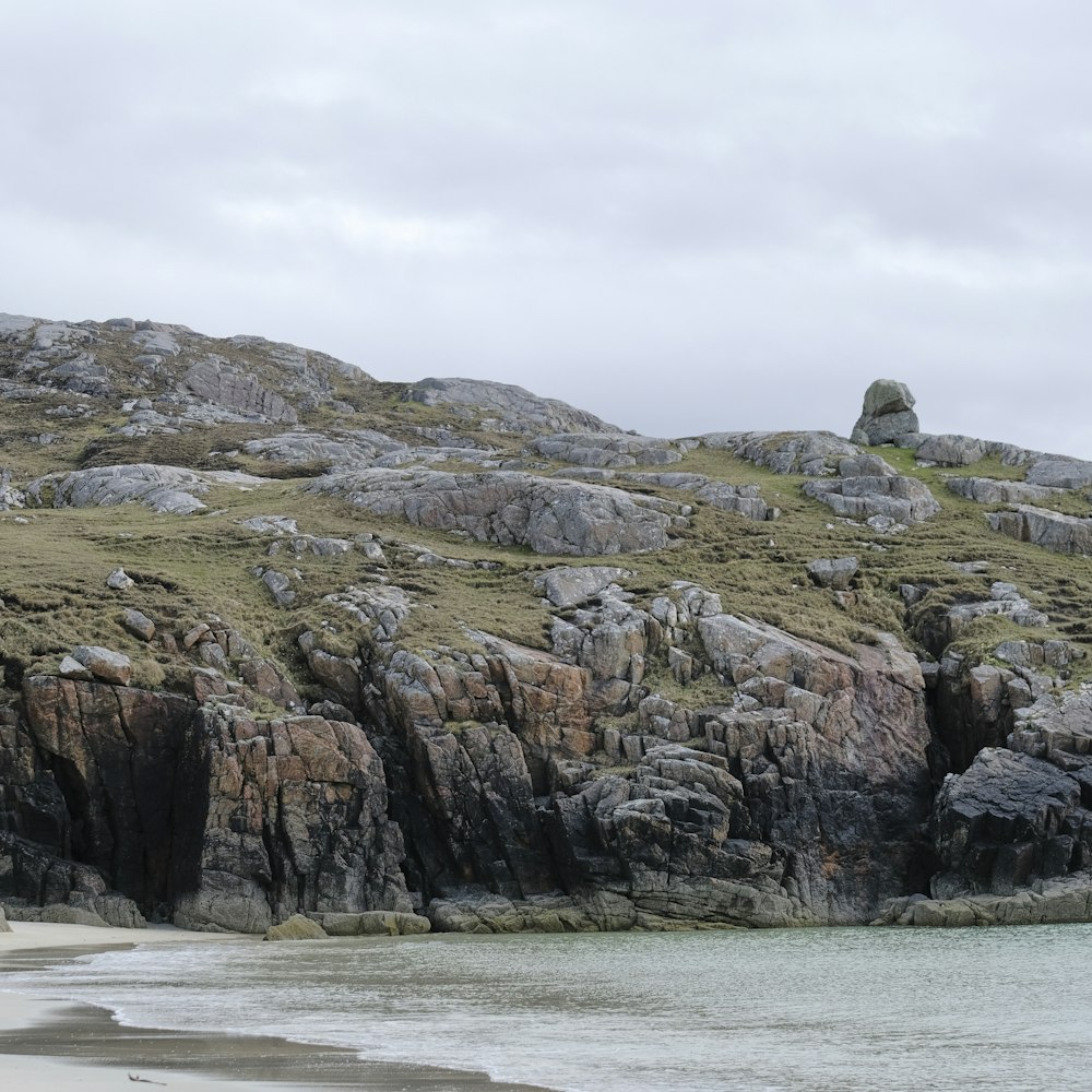 a rocky hill with a body of water in front of it