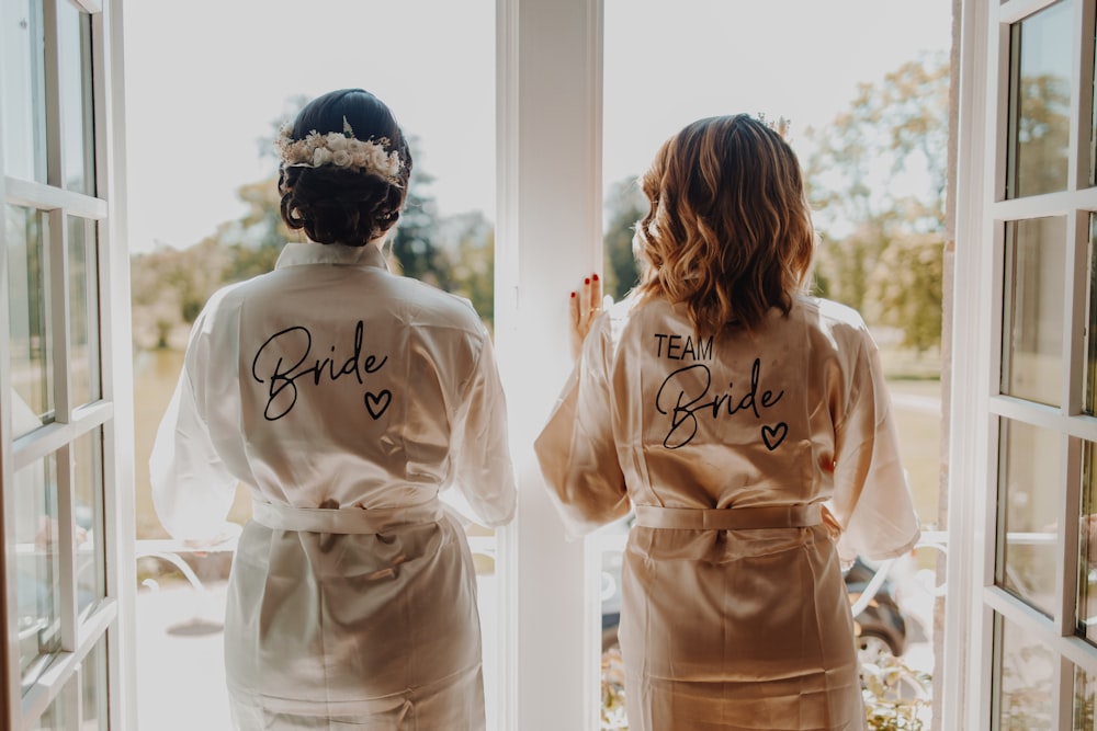 two bridesmaids in robes looking out a window