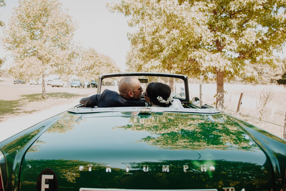 a man and woman kissing in the back of a green convertible