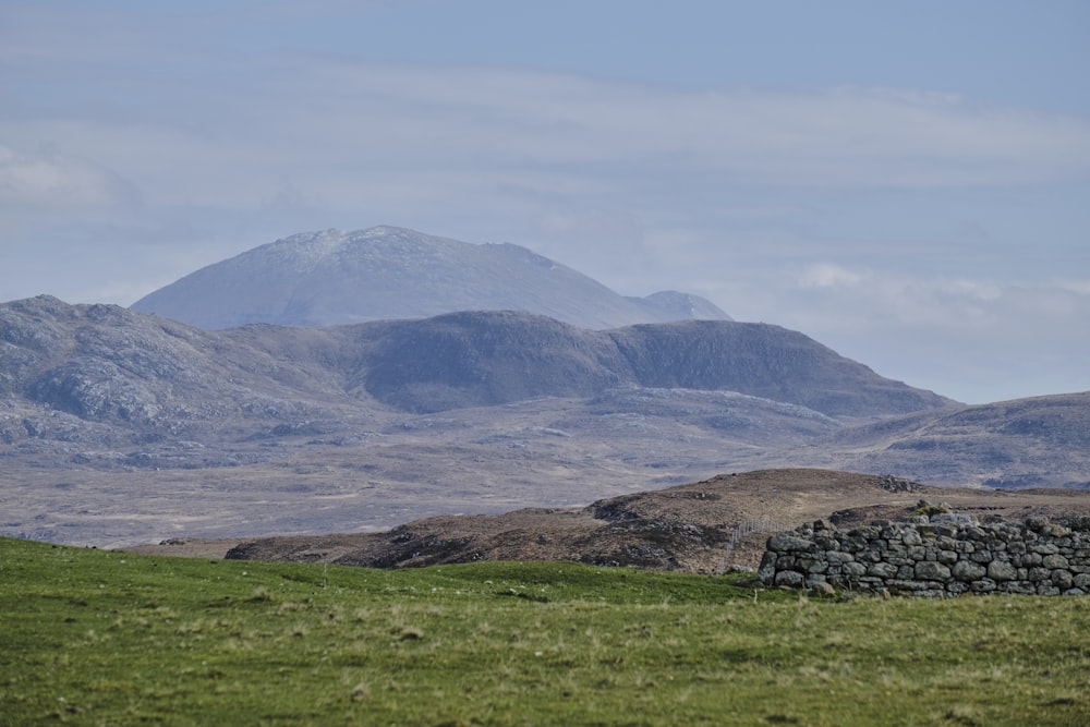 a stone wall in a field with mountains in the background