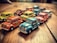 A collection of colorful toy cars is arranged on a wooden surface, featuring vibrant shades of blue, red, yellow, and orange. These miniature, vintage-style cars are lined up closely together, exhibiting a playful and nostalgic atmosphere.