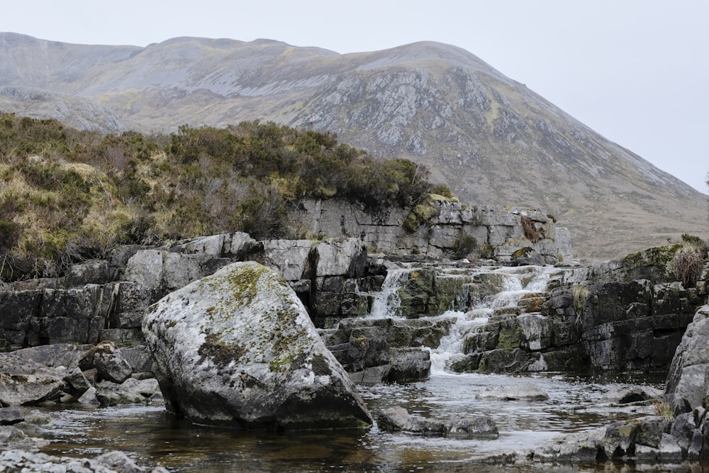 a stream running through a rocky landscape with a mountain in the background