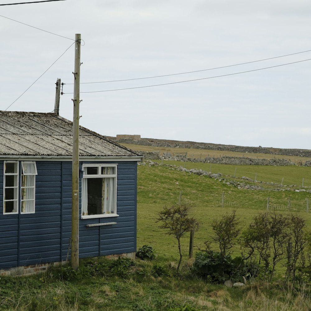 Una piccola casa blu seduta in cima a un campo verde lussureggiante