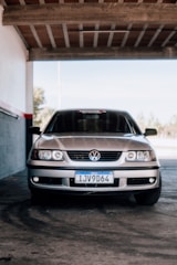 A silver Volkswagen car is parked inside a shaded garage area. The front view highlights the vehicle's headlights, grille, and license plate.