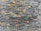 A textured stone wall composed of rectangular slate tiles with varying shades. The stones are stacked horizontally, showcasing a mix of natural grey and brown tones.