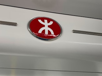 A circular emblem features a stylized red and white symbol, mounted against a white and metallic background.