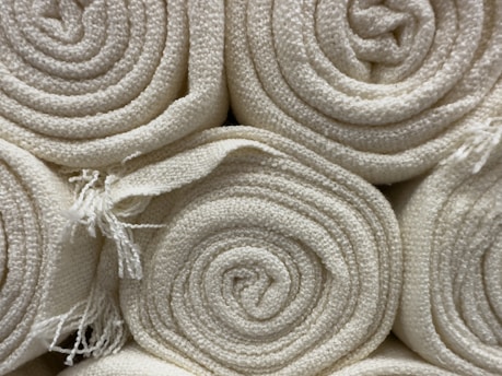 Close-up of finely woven fabric rolls in neutral tones stacked in a factory setting.
