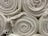 Neatly rolled stacks of off-white textured fabric or cloth are arranged closely together. Frayed edges are slightly visible, giving a natural and raw appearance.