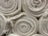 Neatly rolled stacks of off-white textured fabric or cloth are arranged closely together. Frayed edges are slightly visible, giving a natural and raw appearance.
