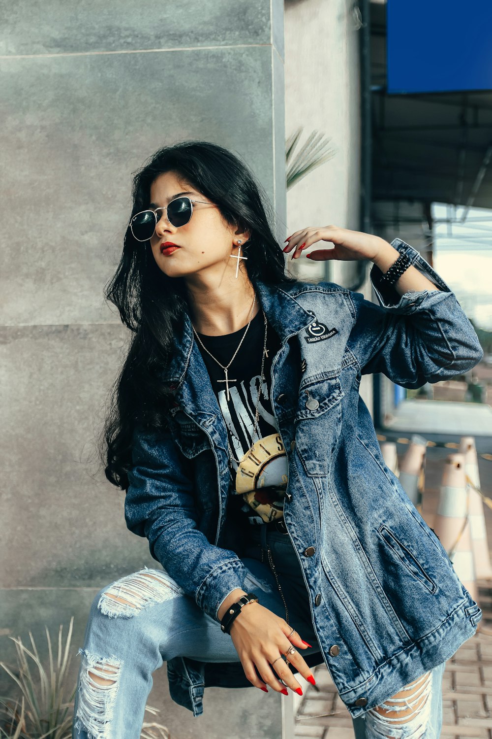 a woman sitting on a wall wearing a jean jacket