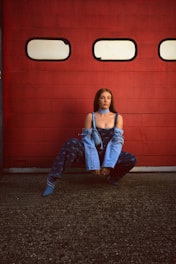 a woman sitting on the ground in front of a red wall
