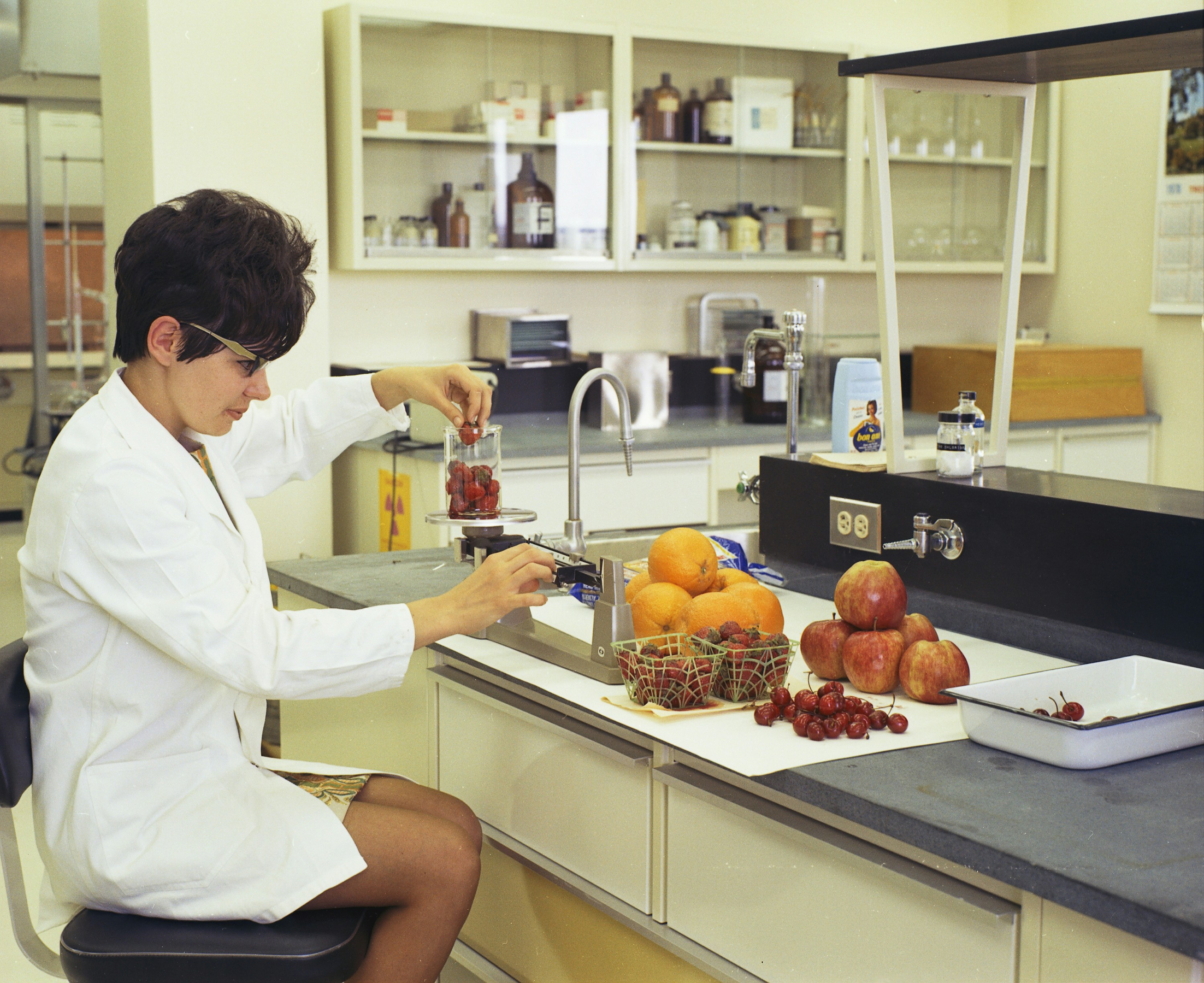 a woman in a white lab coat sitting at a counter in front of a sink