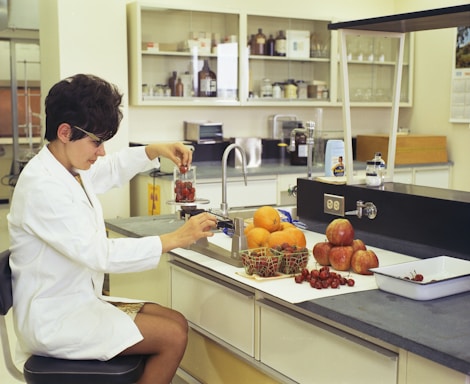 a woman in a white lab coat sitting at a counter in front of a sink