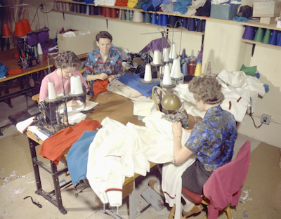 a group of women sitting at a table working on sewing
