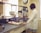 A laboratory setting with a person wearing a white lab coat working at a counter. There are trays of eggs, jars, and laboratory equipment, including a mixer and a clock on the wall.