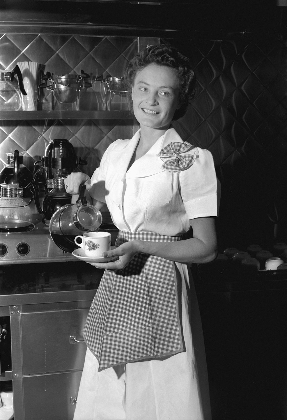 a woman in an apron holding a cup in a kitchen