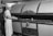 A baker dressed in white uniform and cap uses a long-handled peel to place or retrieve bread from a large industrial oven labeled 'Master Baker Oven'. The setting appears to be a bakery or a baking manufacturing facility.