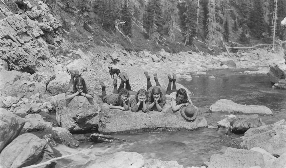 a group of people sitting on top of a rock next to a river