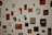 A collection of various artworks and objects mounted on a white wall. The pieces include abstract designs, photographs, and mixed media art, predominantly in red, black, and white colors. Some items are set in frames while others are standalone objects like plates or small sculptures.