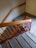 A staircase with stone steps and black anti-slip strips runs down the image. The railing is made of wood and metal, with the wood painted in a light brown and the metal in a red hue. The walls and floor are a light gray, adding a muted tone to the scene.