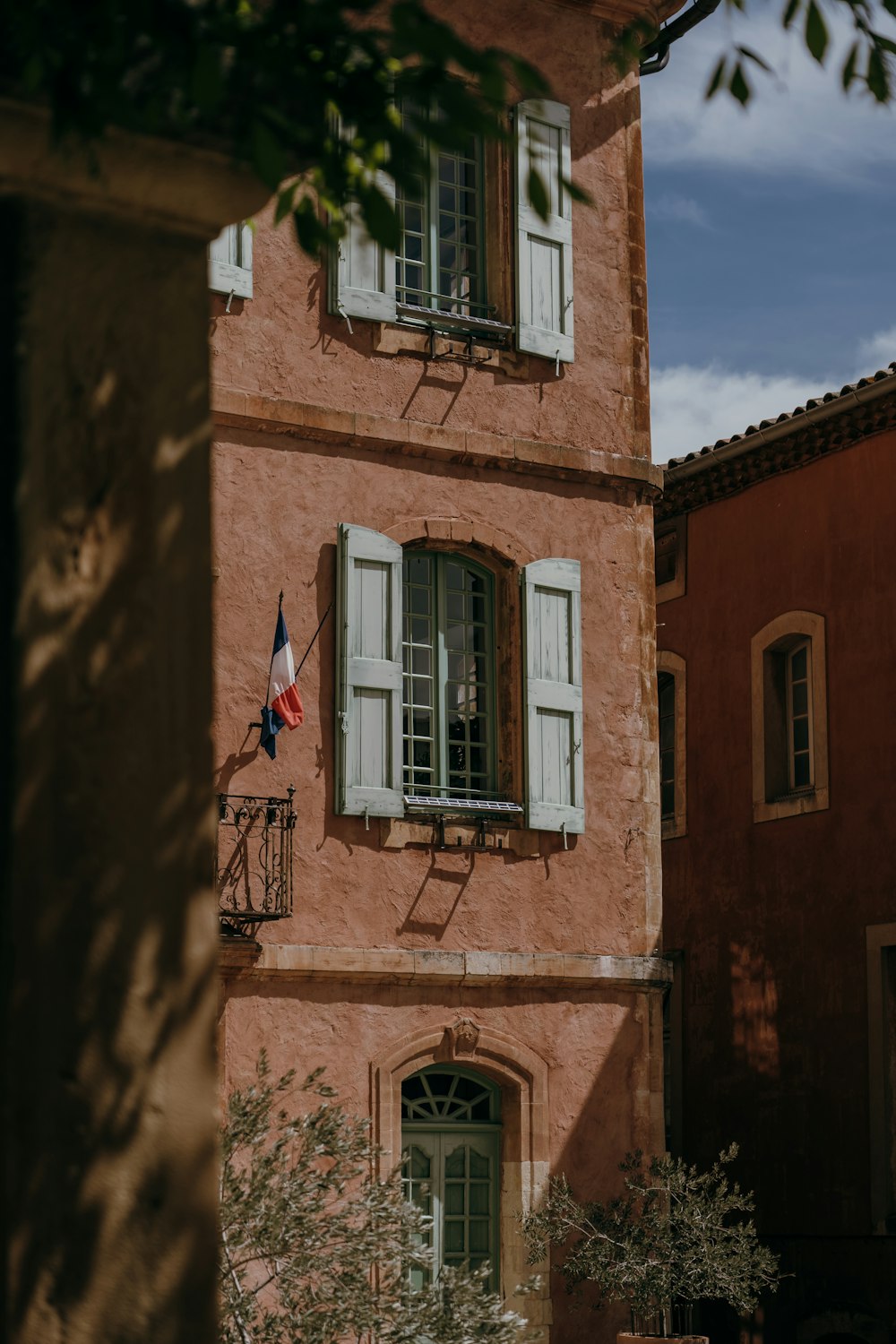 a tall pink building with white shutters and a flag hanging from it's