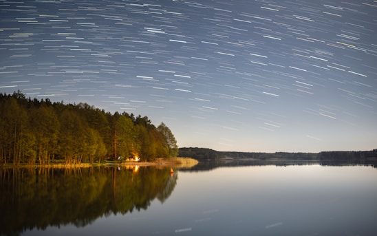 A serene night scene showing a camera on a tripod pointed at a star-filled sky with visible light trails.