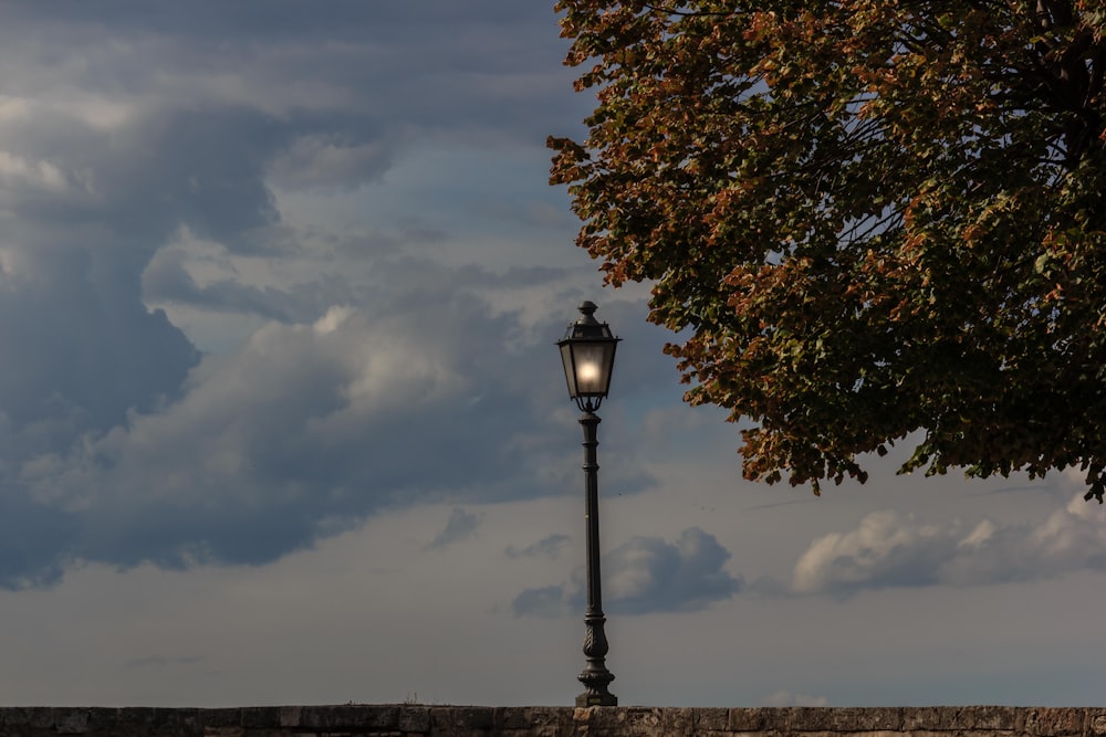 a street light next to a stone wall under a cloudy sky