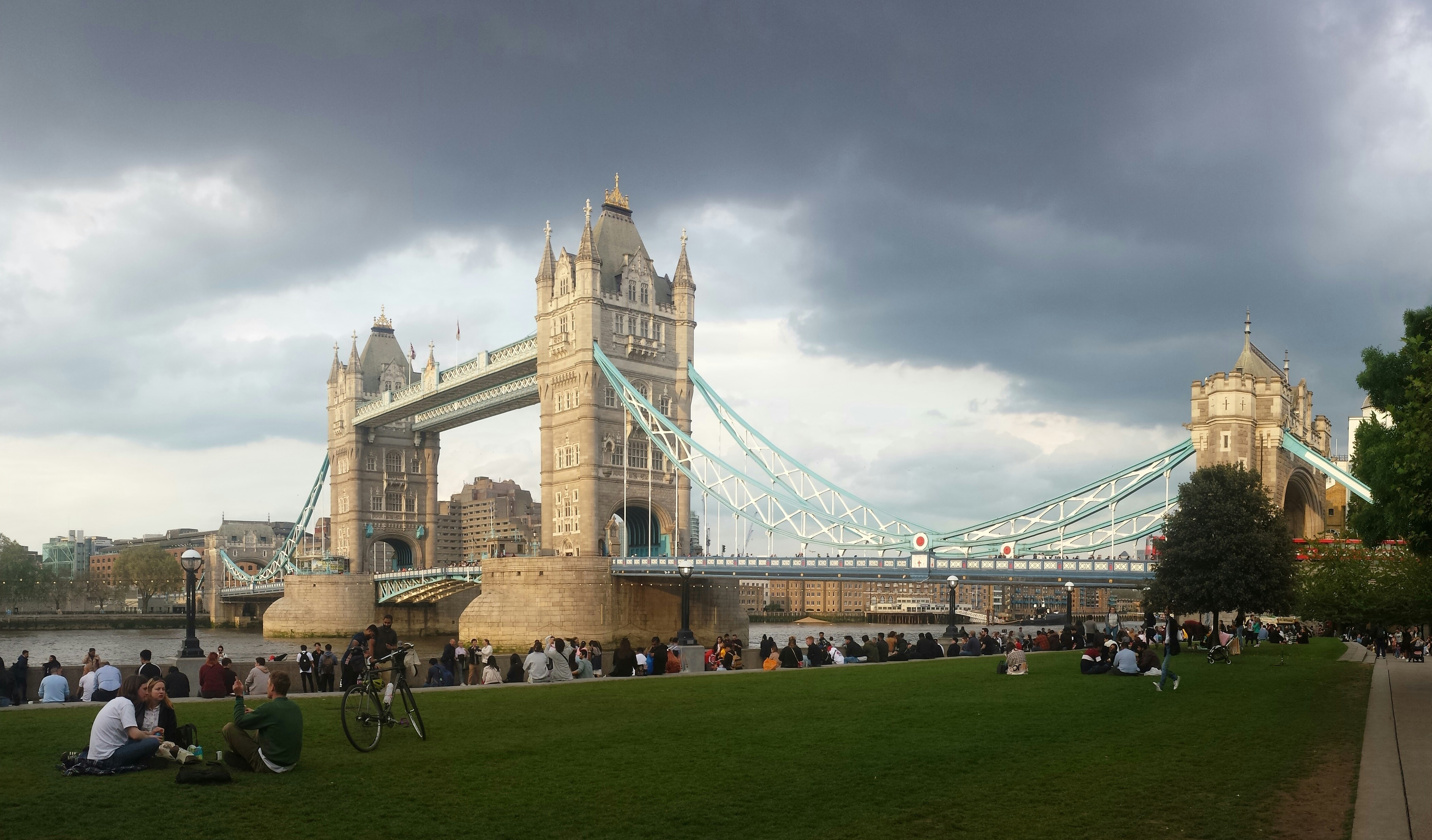 a group of people sitting on the grass in front of a bridge