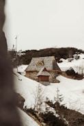 A modern prefabricated cottage nestled on a rocky hillside with snow atop its roof.