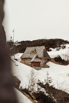 A modern prefabricated cottage nestled on a rocky hillside with snow atop its roof.