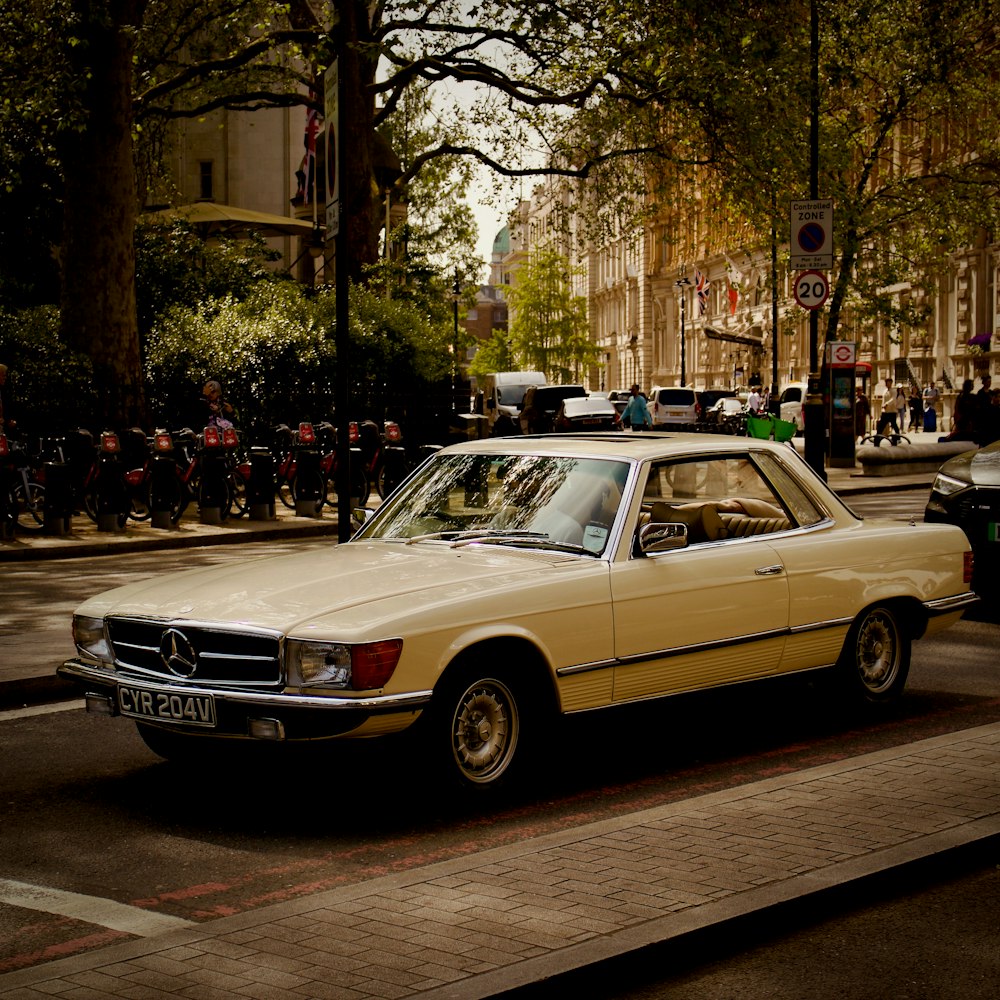 a yellow car driving down a street next to tall buildings