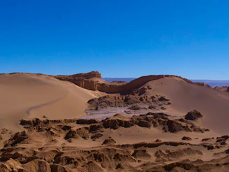 A vast expanse of the Namib Desert with towering orange sand dunes under a clear blue sky.