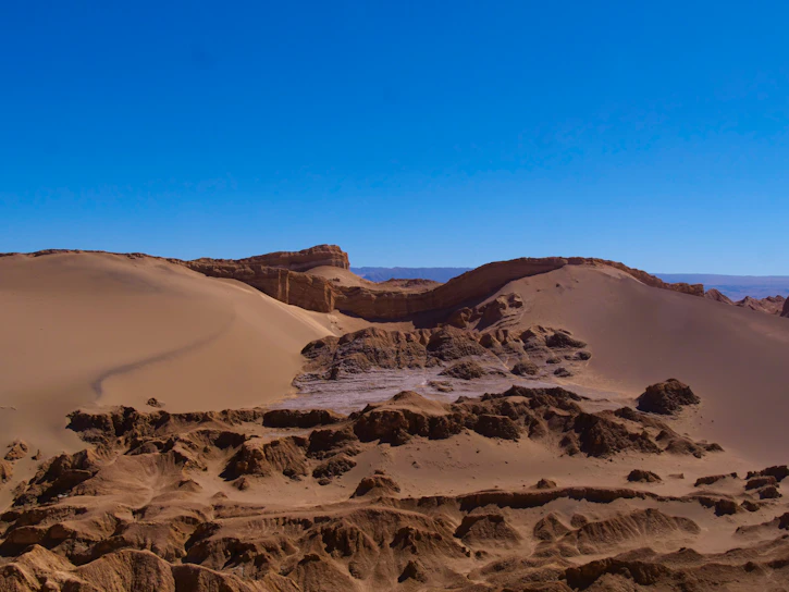 A vast expanse of the Namib Desert with towering orange sand dunes under a clear blue sky.